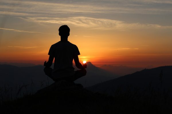 silhouette of man meditating on rock cliff during golden hour